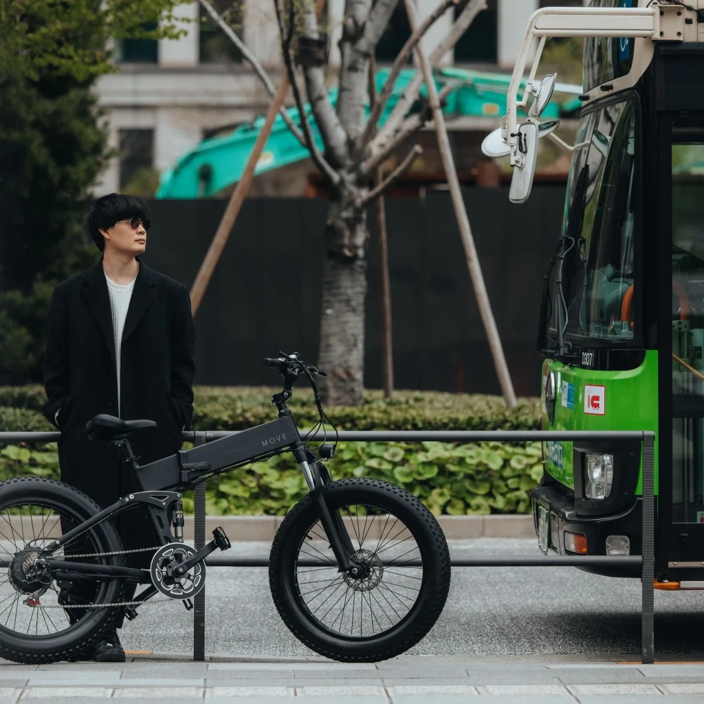 電動自転車とサングラスをかけた男性がバス前でたたずむ