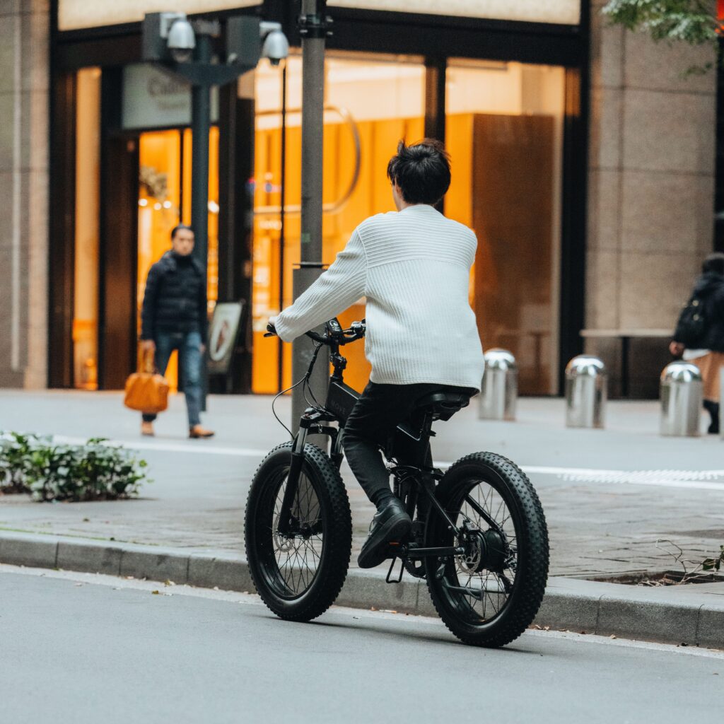 電動自転車にのっておしゃれなビル街を向こう側へ走っていく男性