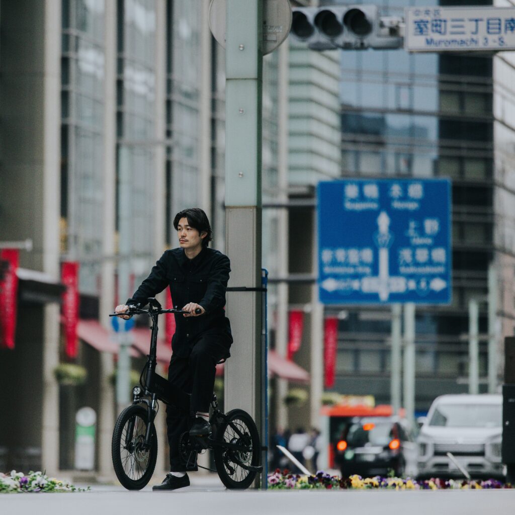 電動自転車にのって東京の交通量の多い道路で走っている男性